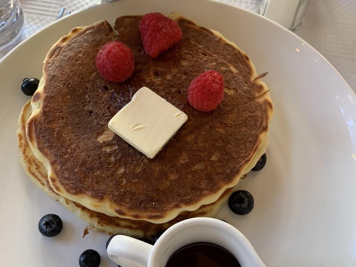 Stack of buttermilk pancakes with butter, raspberries, blueberries, and maple syrup