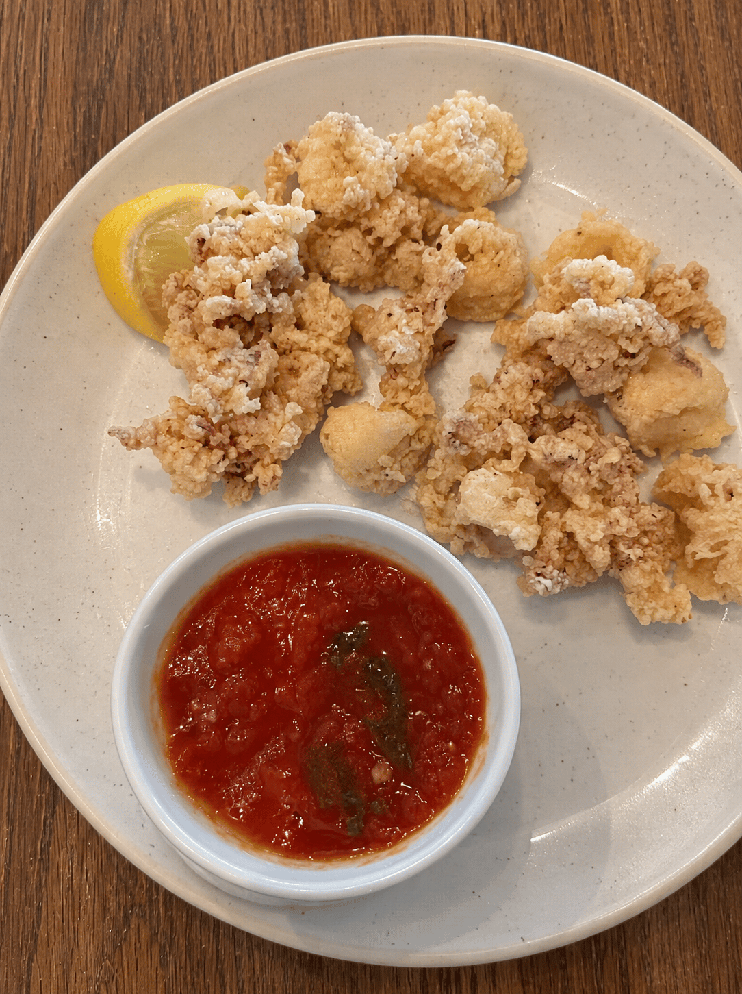 Lightly battered fried calamari with a lemon wedge and a bowl of marinara sauce on a ceramic plate