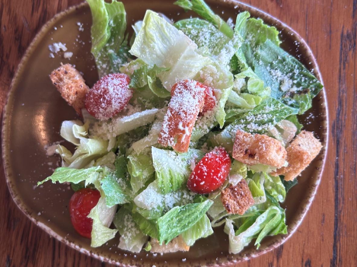 Caesar side salad with romaine, grape tomatoes, grated Parmesan, and garlic croutons on a brown plate