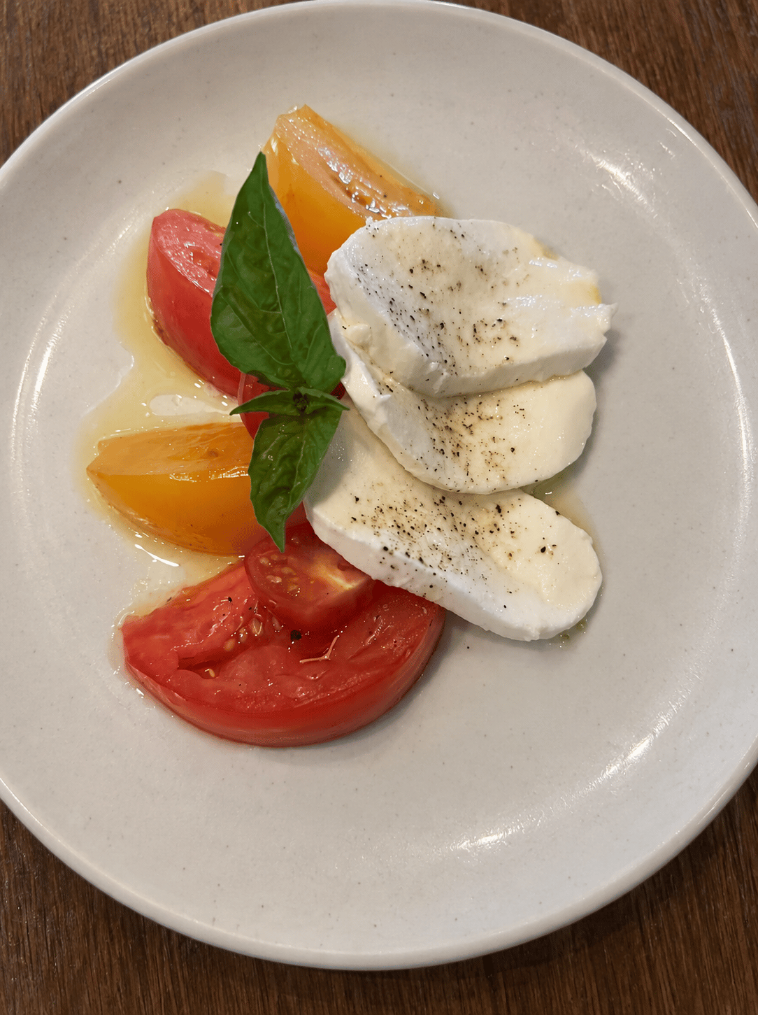 Red and yellow heirloom tomato wedges with three slices of fresh mozzarella and basil on a ceramic plate