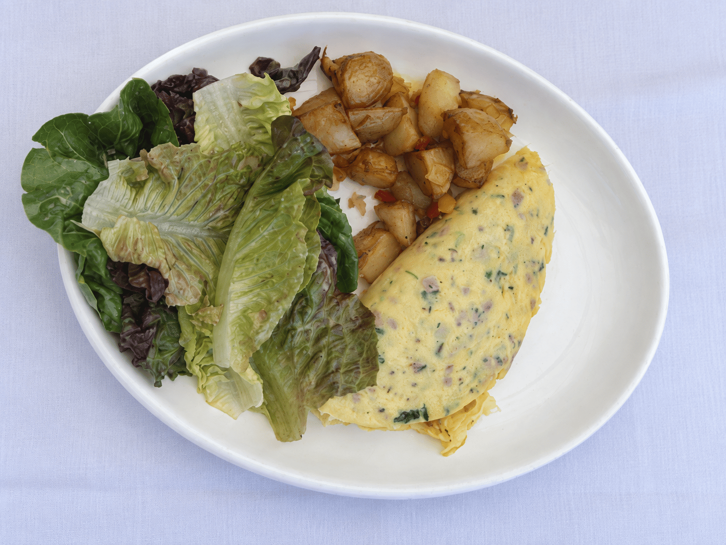 Tortilla doblada con motitas rosas y verdes, patatas doradas con pimientos y ensalada verde