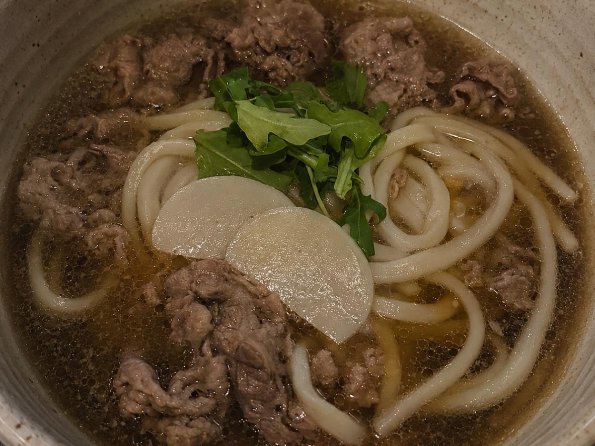 Niku udon with sliced beef, thick noodles, greens, and fish cake in clear broth