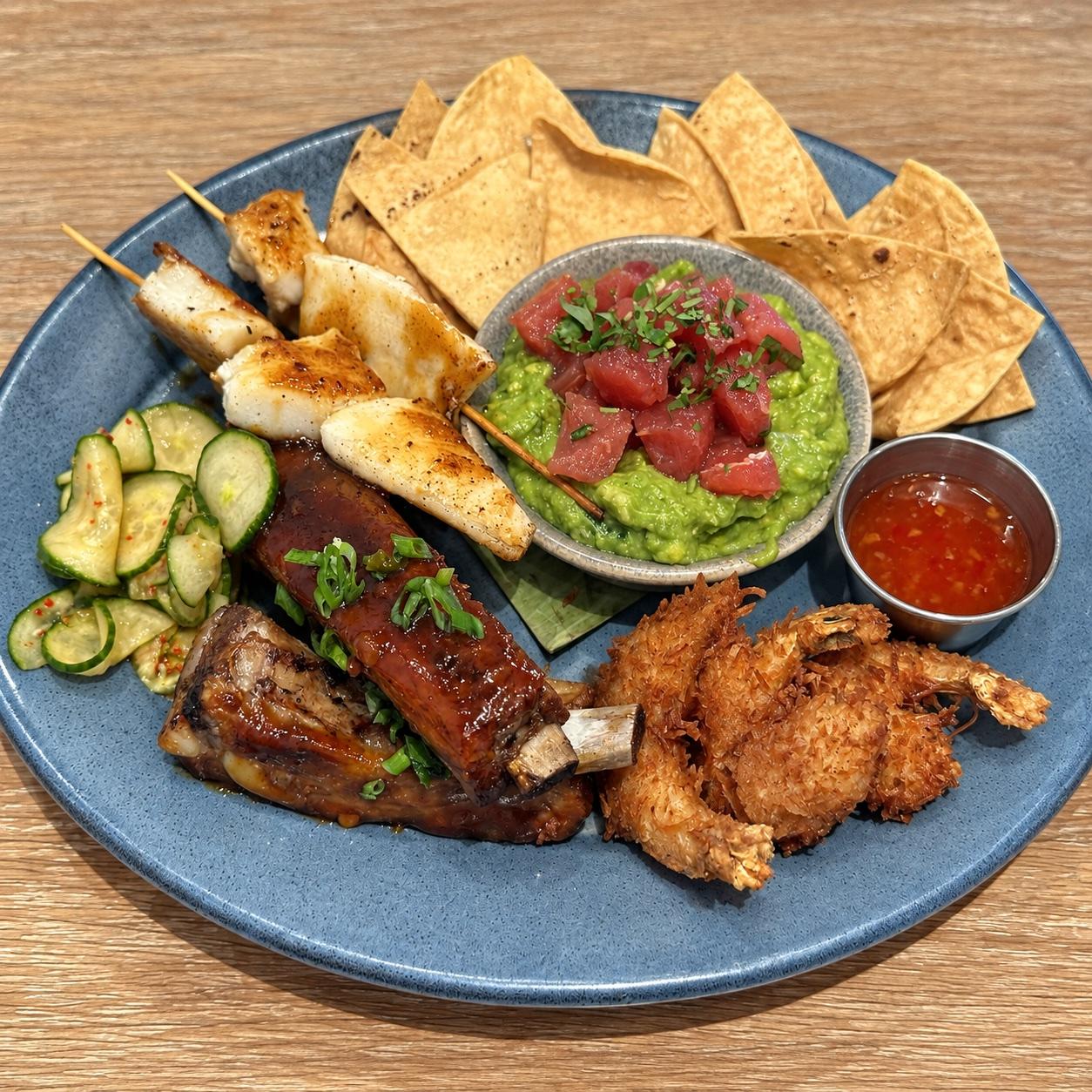 Pupu platter with coconut shrimp, glazed ribs, sea bass skewers, guaca-poke, tortilla chips, and cucumber salad