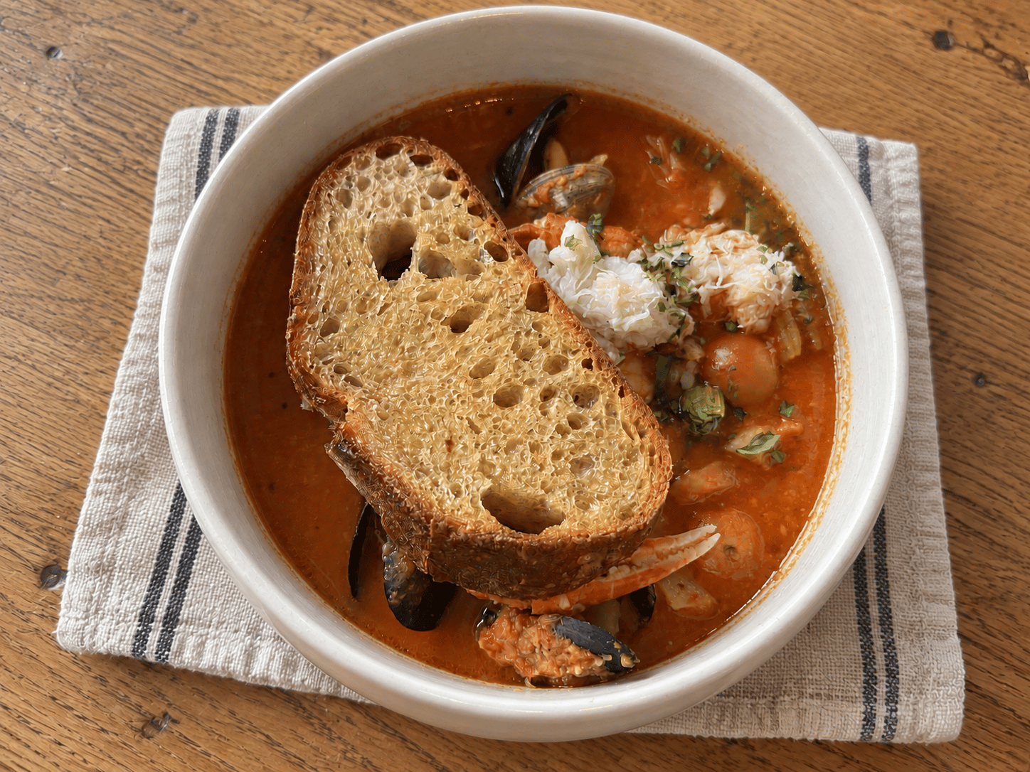 Cioppino with crab, mussels, clams, and toasted sourdough in a white ceramic bowl.