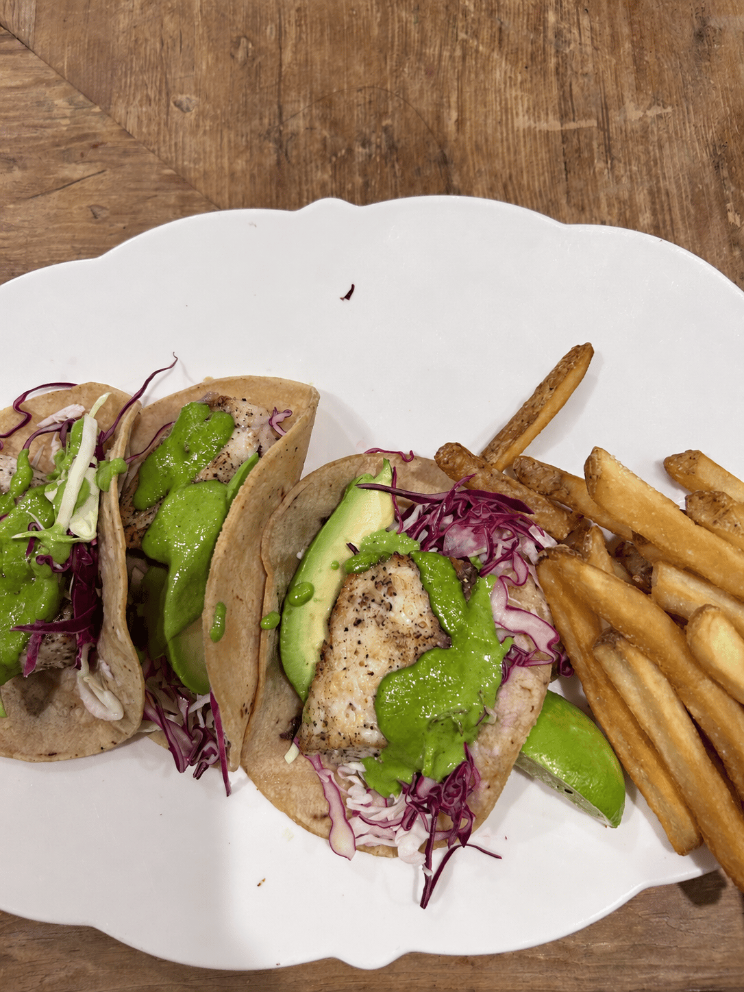 Fish tacos with cabbage slaw, avocado slices, and green cilantro crema, served with fries and lime
