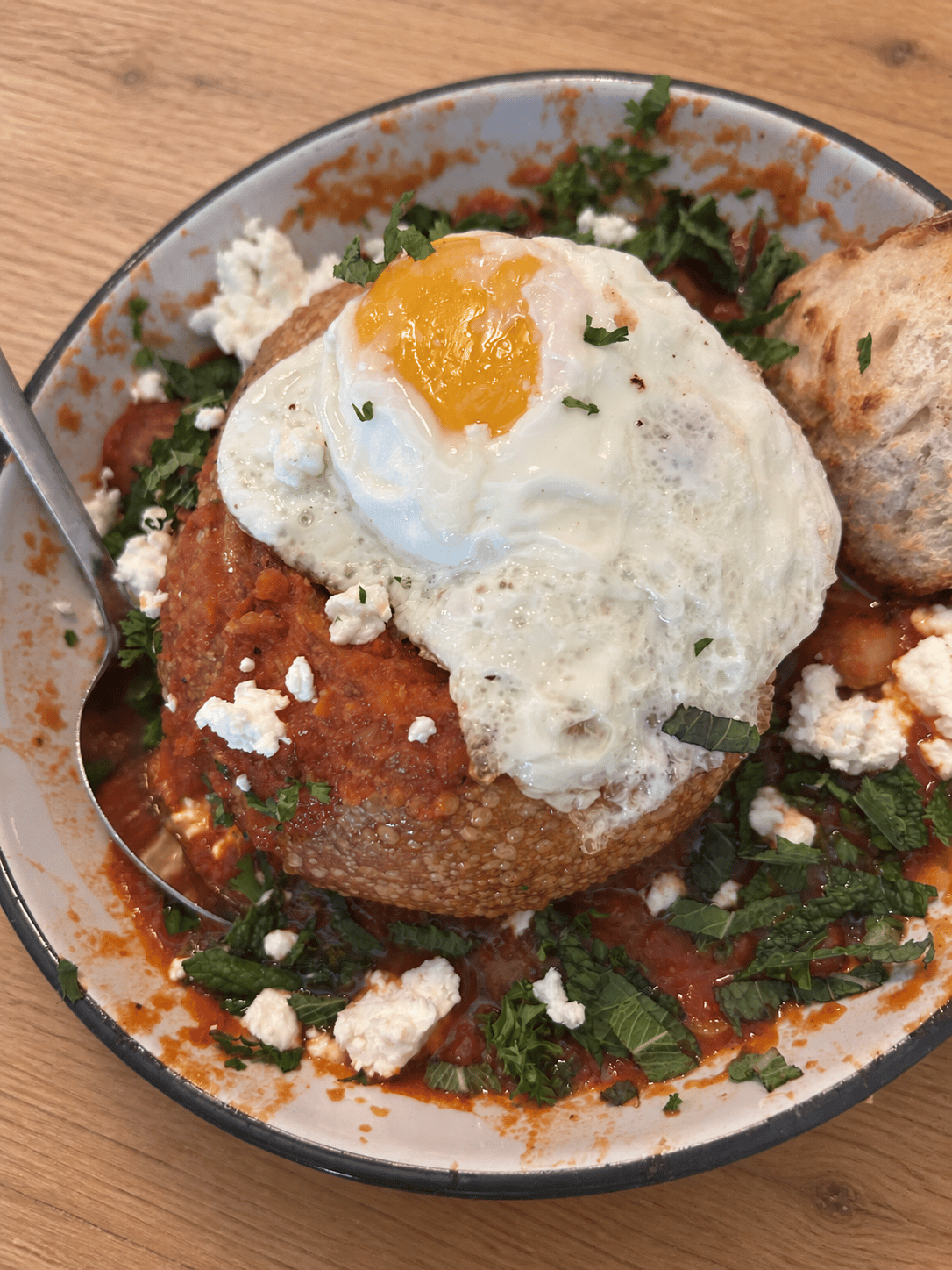 Shakshuka bread bowl with mushroom tomato sauce, feta, mint, scallions, and a runny fried egg.