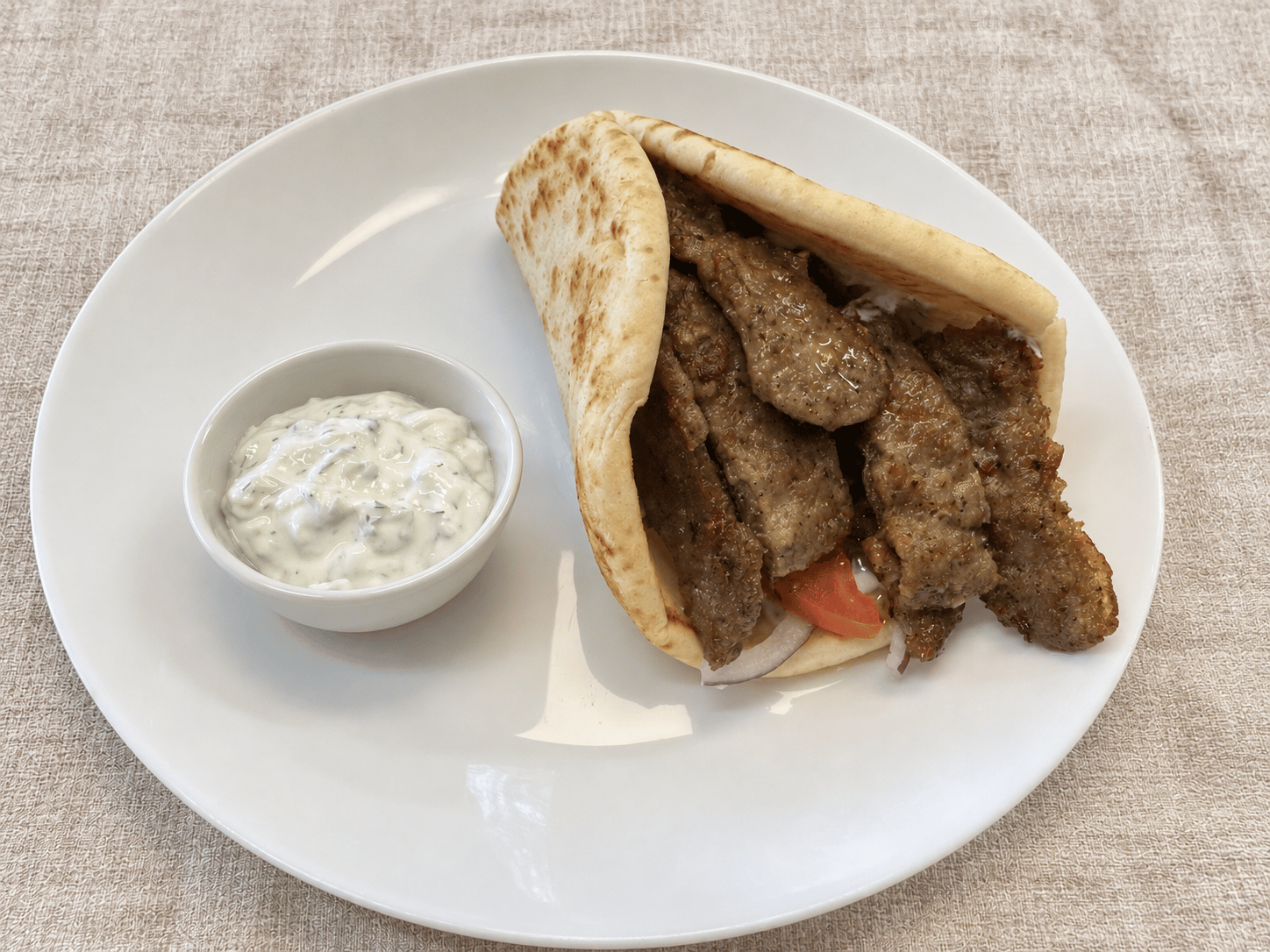 Beef gyro meat in folded pita with tomato and red onion, with a cup of cucumber tzatziki alongside
