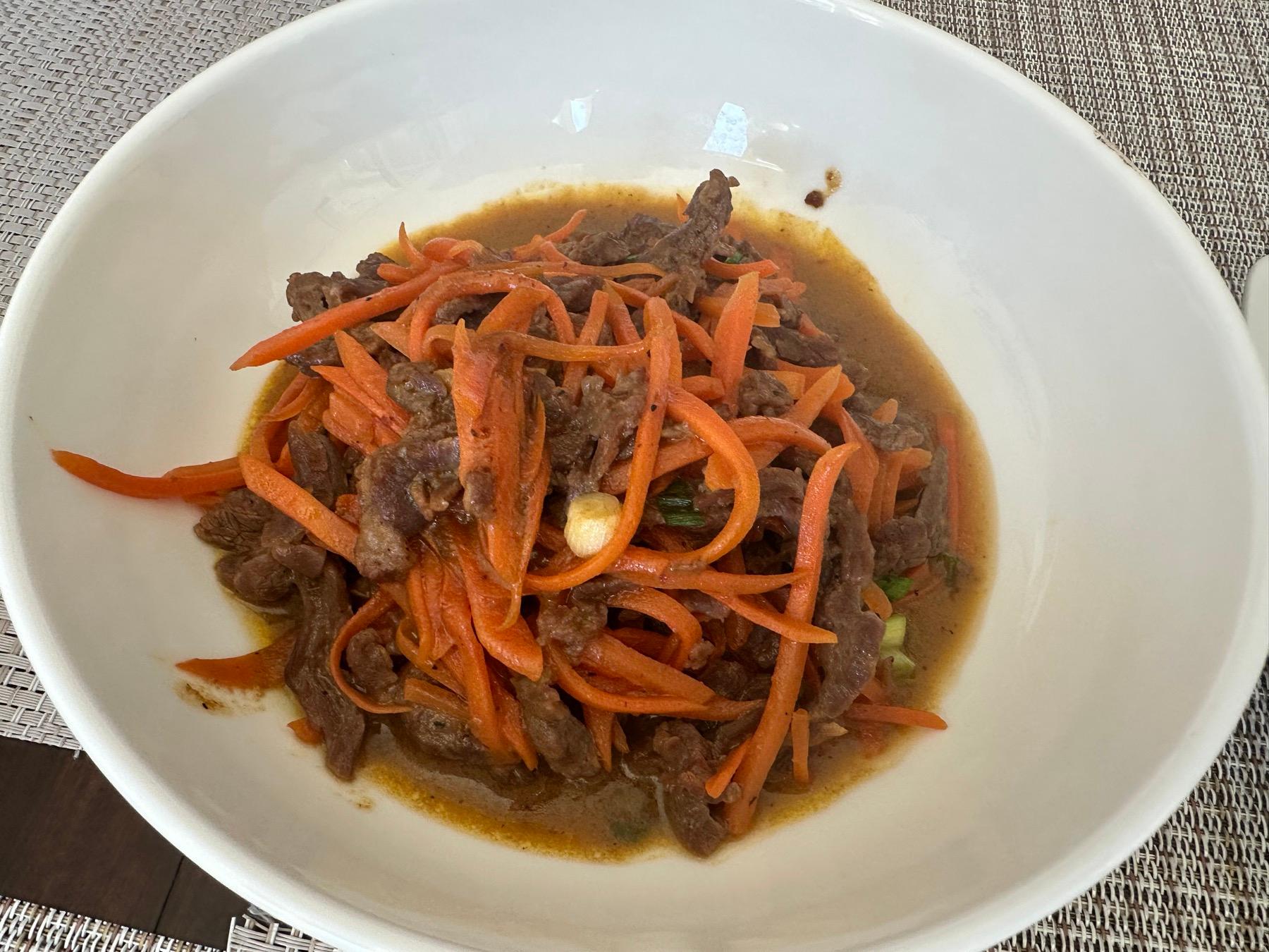 Homemade beef and carrot stir-fry with thin orange carrot strips and scallions in a white bowl