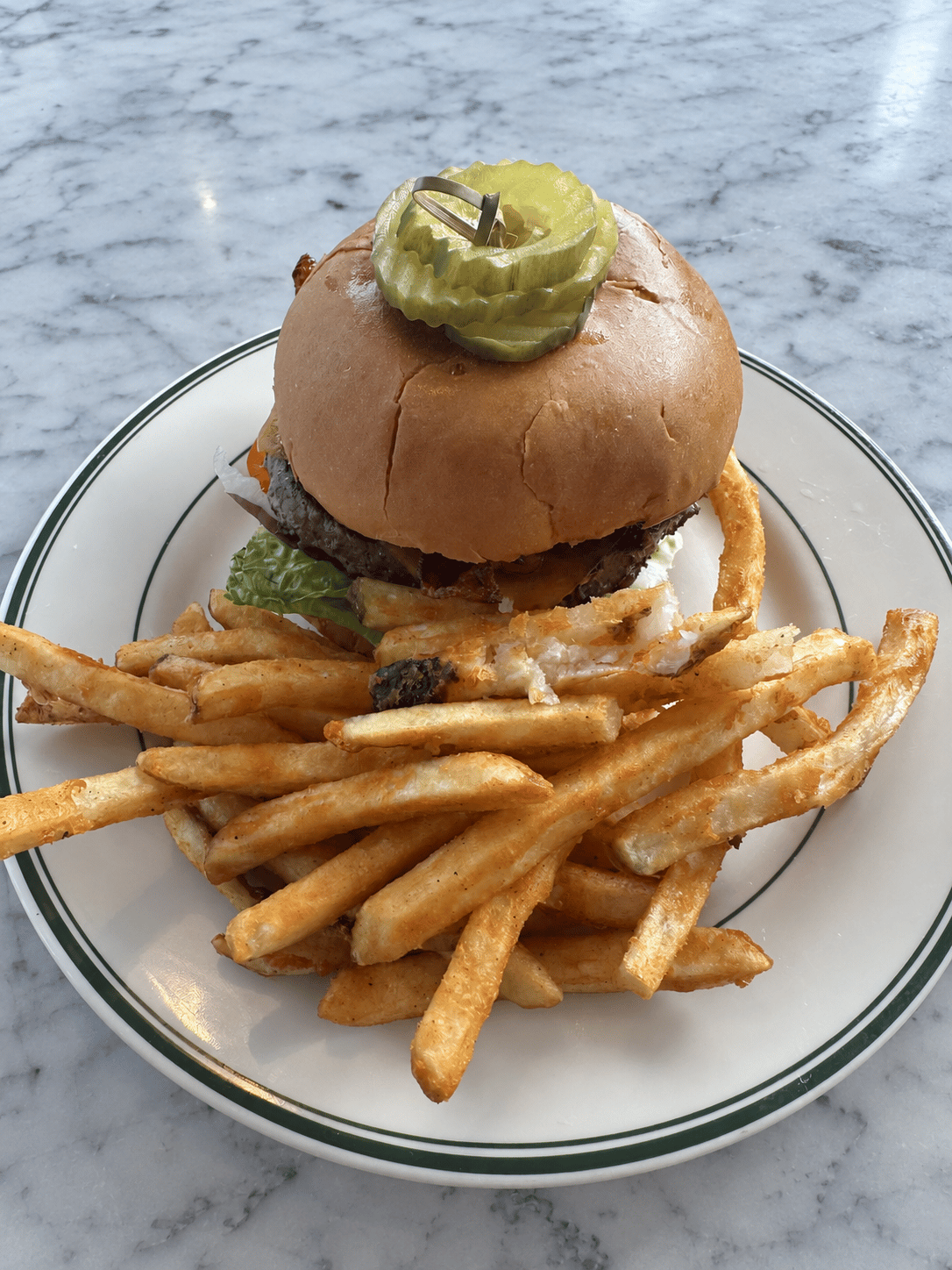 Breakfast cheeseburger with bacon, fried egg, lettuce, tomato, red onion, and pickles, served with fries