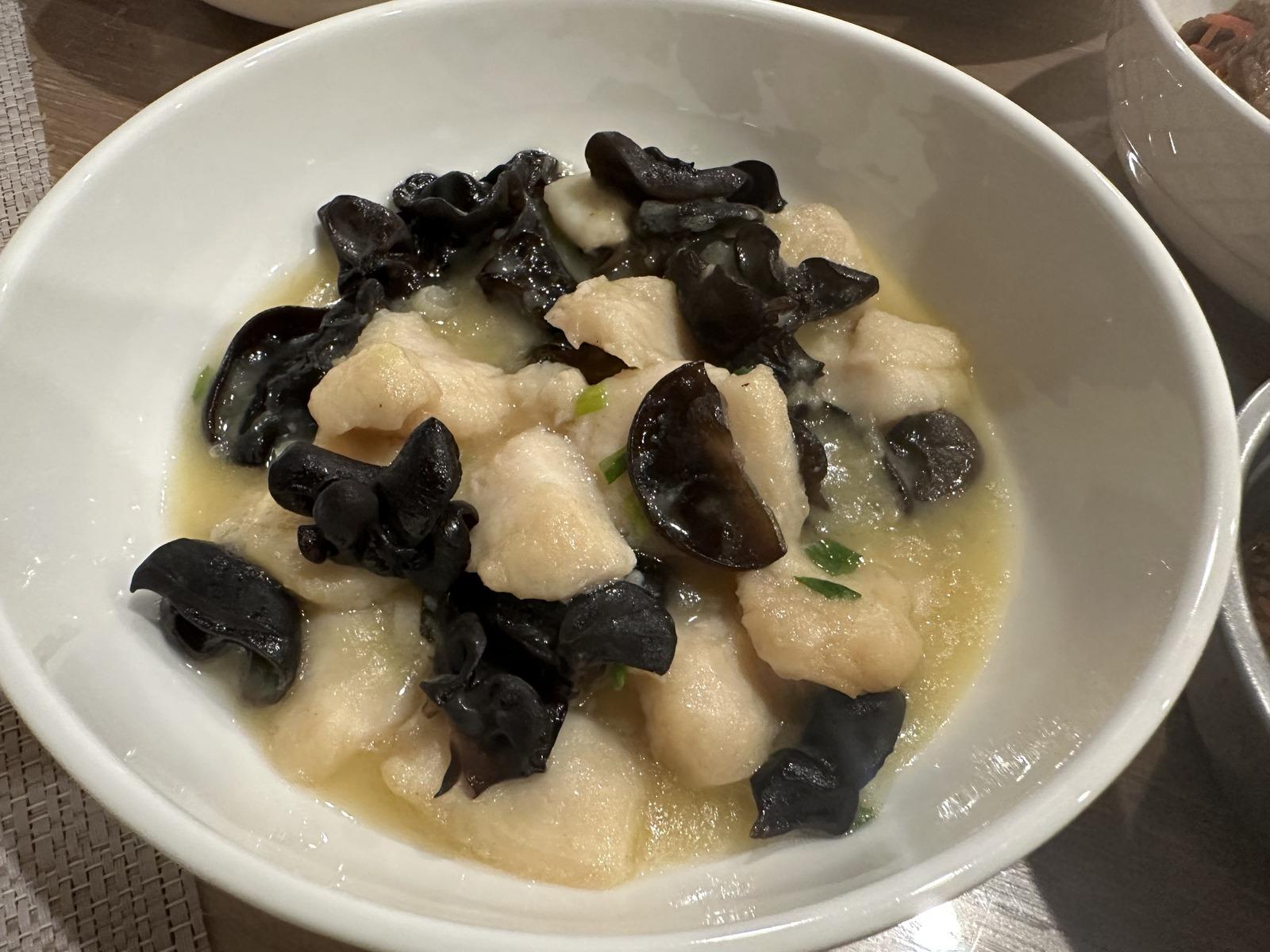 White fish pieces and black wood ear mushrooms in a light glossy sauce with scallions in a white bowl