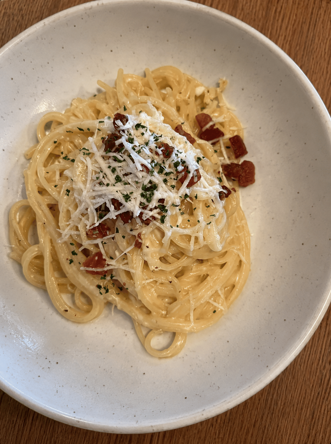 Espaguetis cremosos con tocino, parmesano rallado y perejil picado en un tazón de cerámica