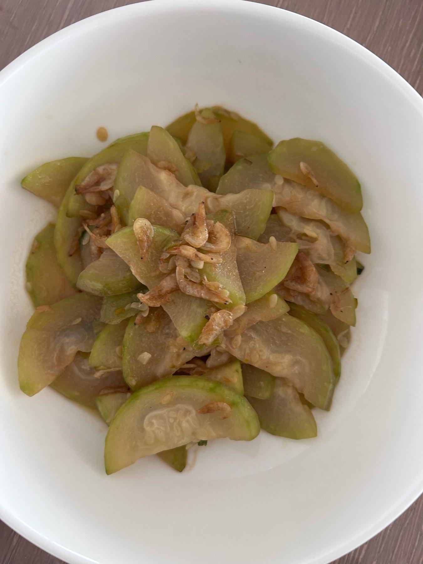Homemade braised fuzzy melon with dried shrimp in a white bowl, with translucent half-moon slices and small pink dried shrimp on top
