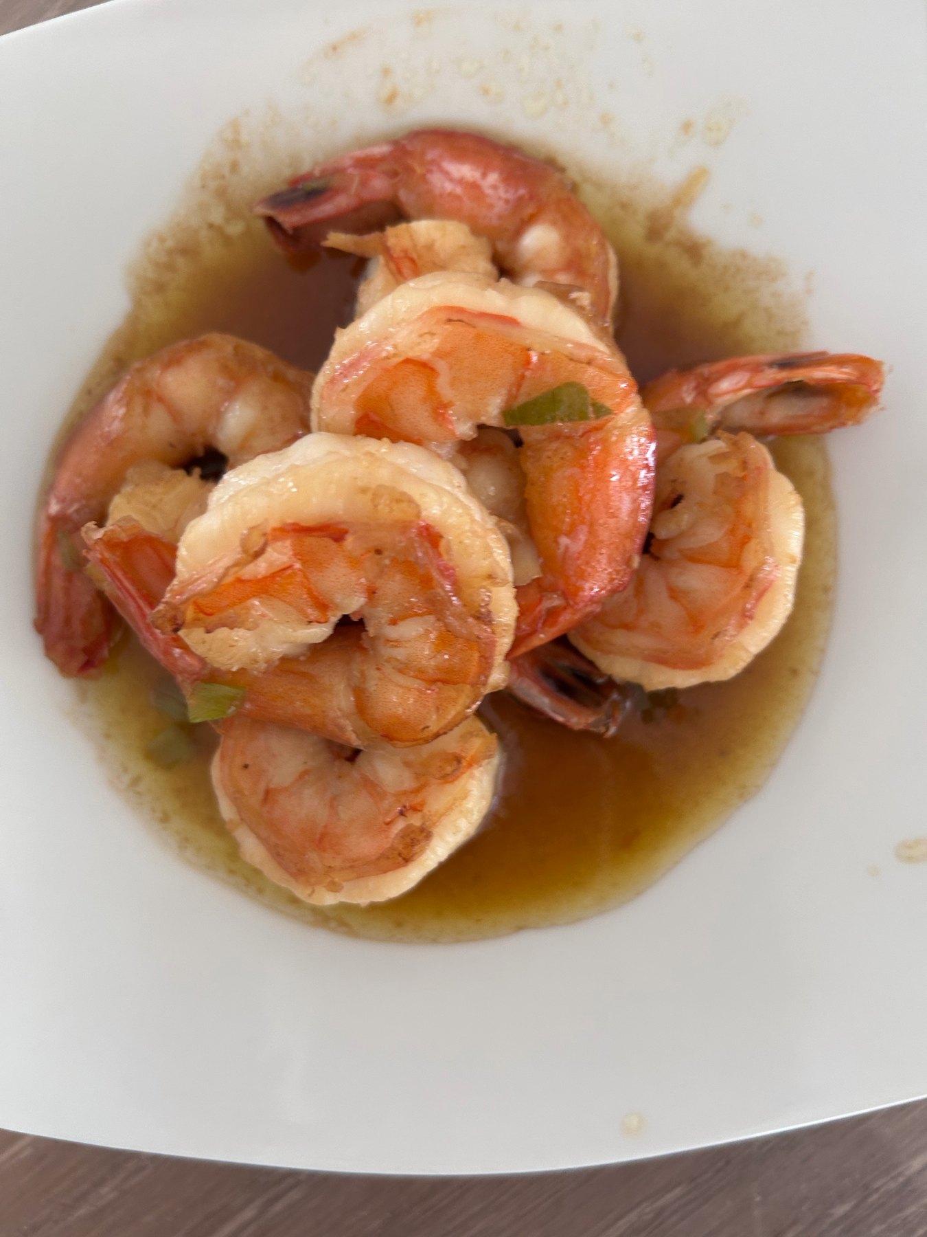 Homemade ginger scallion shrimp, shell-on, in a light amber soy sauce with scallions in a white bowl