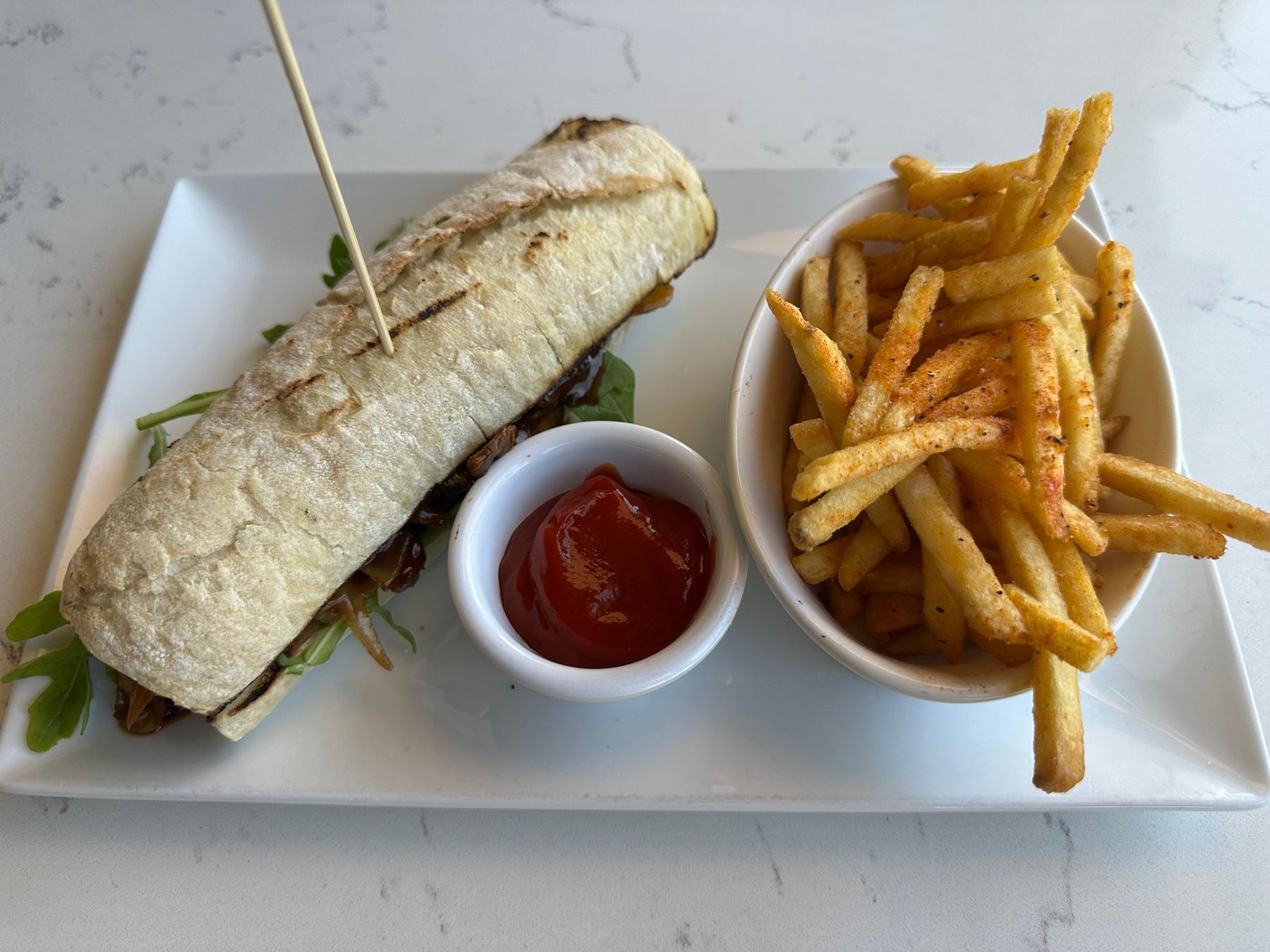 Roast beef dip sandwich with caramelized onions and arugula served with fries