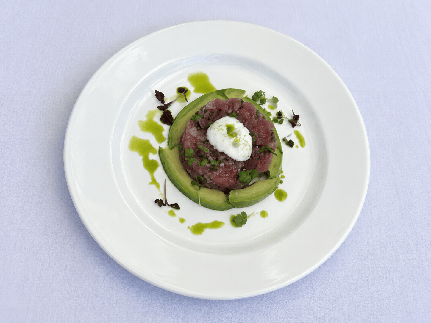 Tartar de atún rodeado de aguacate, con una crema blanca y gotas de aceite de hierbas
