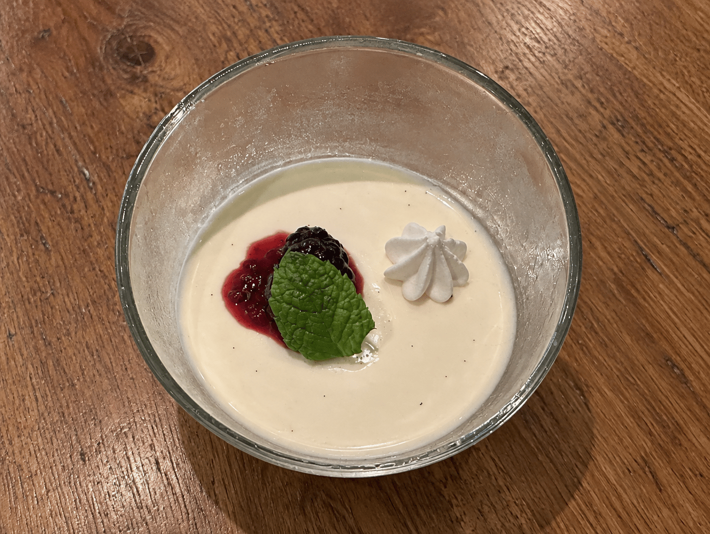 Vanilla-speckled panna cotta in a glass bowl with blackberry compote, a mint leaf, and a small white piped garnish